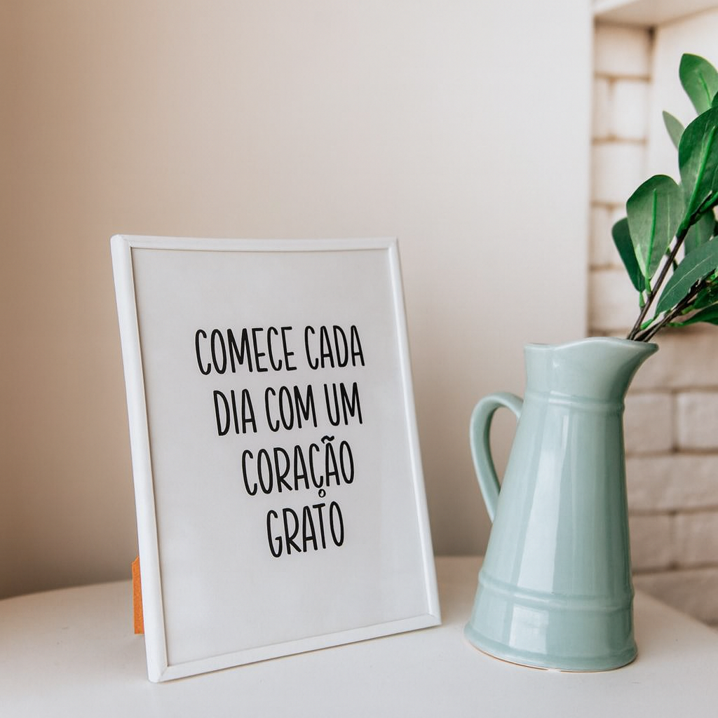 Quadro decorativo com a frase “Comece cada dia com um coração grato” ao lado de uma jarra verde e folhas.